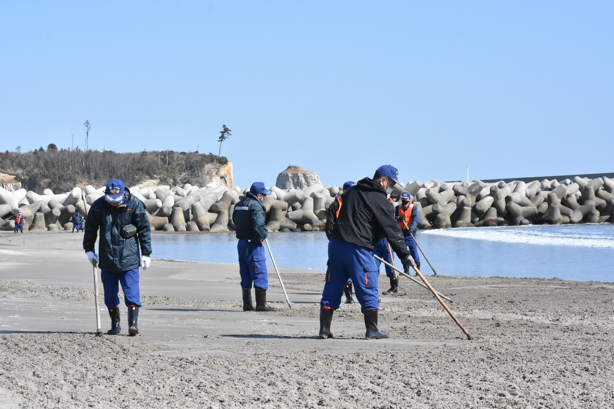 富岡漁港南側の砂浜で捜索活動を行う消防団員
