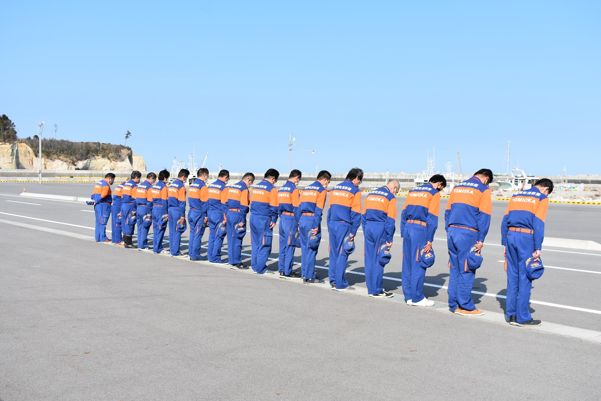 富岡漁港にて犠牲者に黙とうをささげる消防団員（とみおか守り隊）